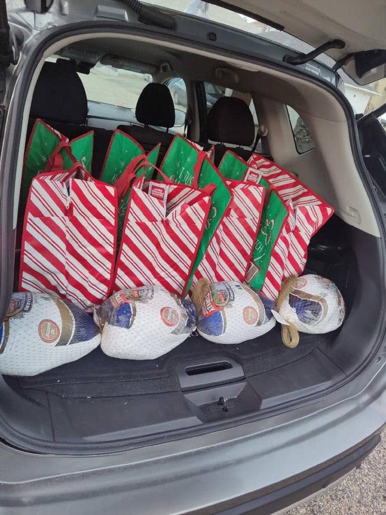 Car trunk filled with holiday gift bags and turkeys for community donations