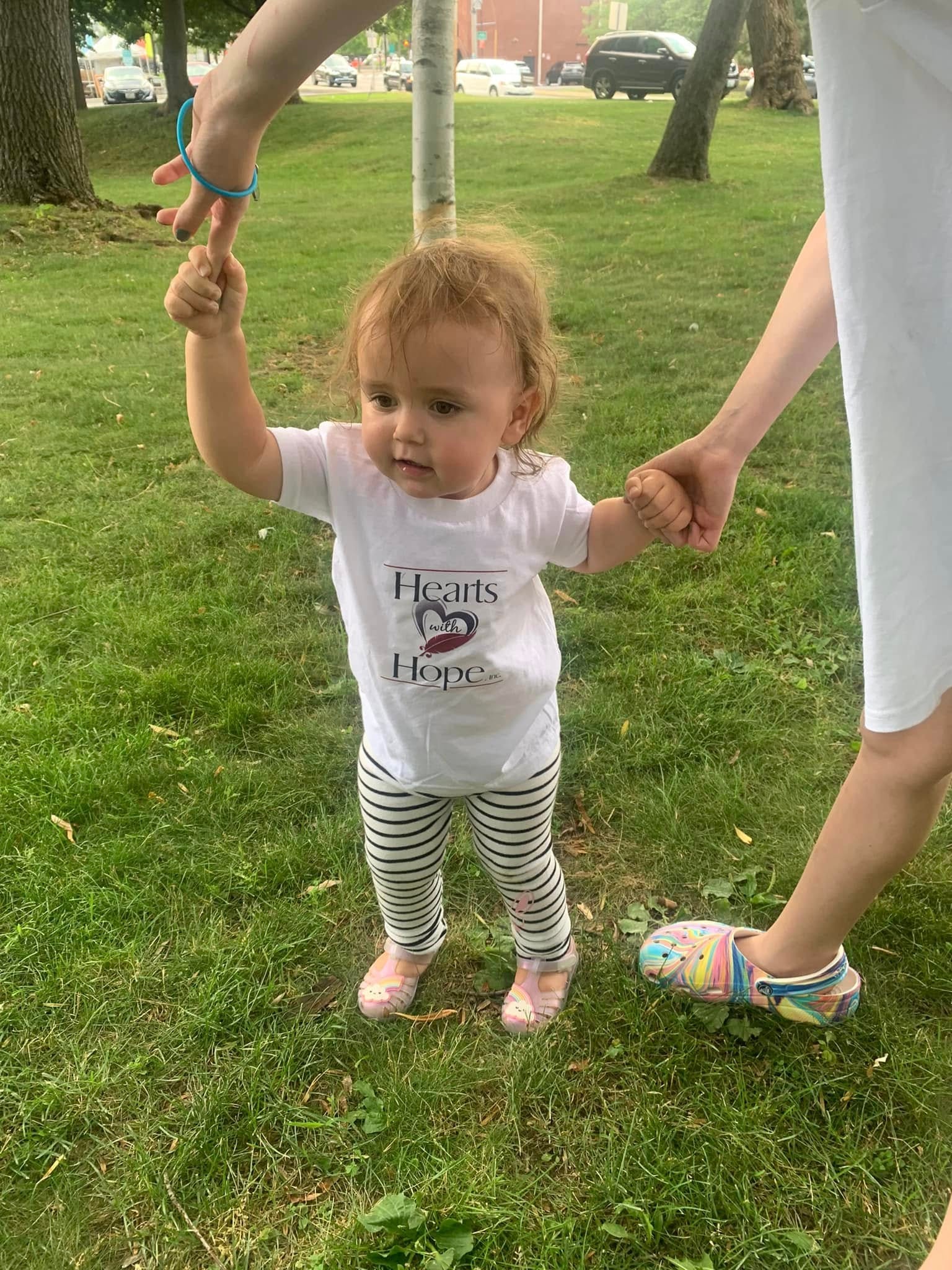 Toddler wearing Hearts with Hope shirt standing on grass at outdoor event