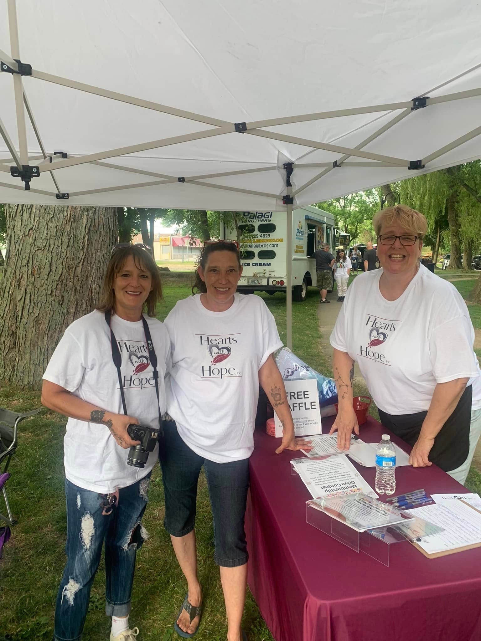 Three Hearts with Hope volunteers in branded shirts at outdoor event tent