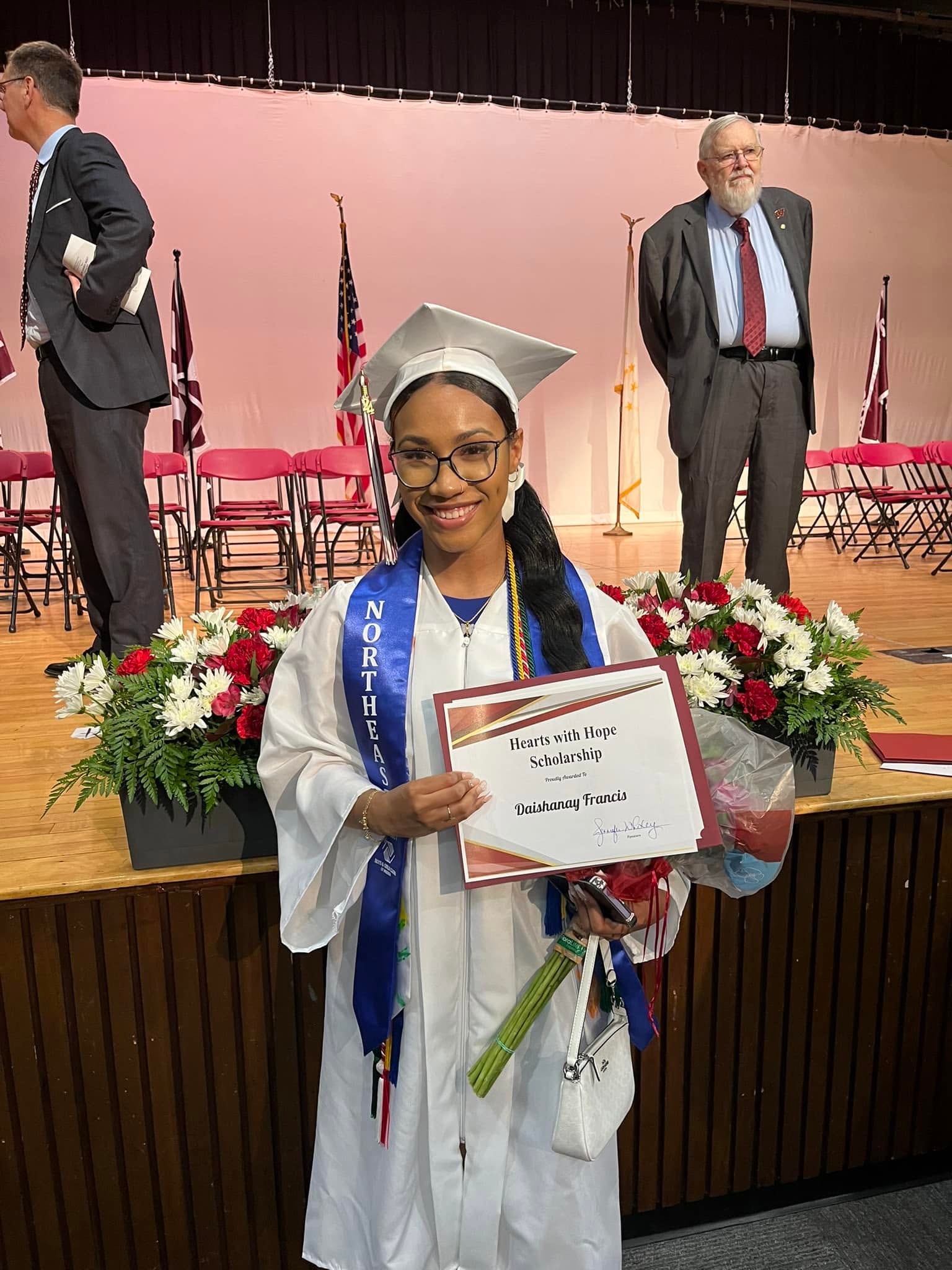 Graduate in cap and gown holding Hearts with Hope scholarship certificate